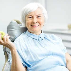 senior woman holding an apple in the dental chair