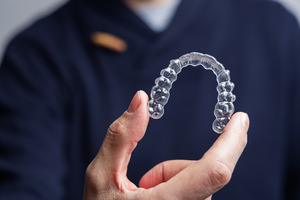 Man with black shirt holding an Invisalign aligner